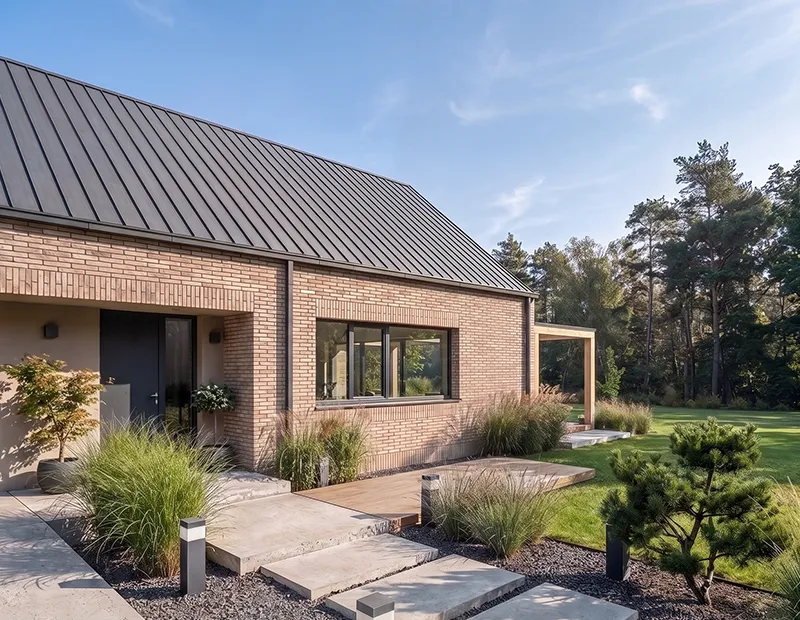 Parterowy dom z cegły z dachem z blachy i ścieżką wejściową wśród zieleni – projekt TRINN architekci